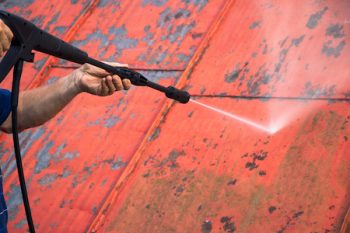 Man Is Washing The Roof With A High Pressure Washer. Worker Cleaning A Red Metal Sheet Roof By Water. Detail