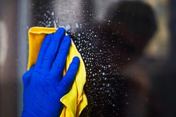 A Woman Or Man Washes A Window At Home. House Cleaning. Washing Dirty Window Glass Detergent For Window Washing Wearing Blue Mittens And A Yellow Cloth Rag